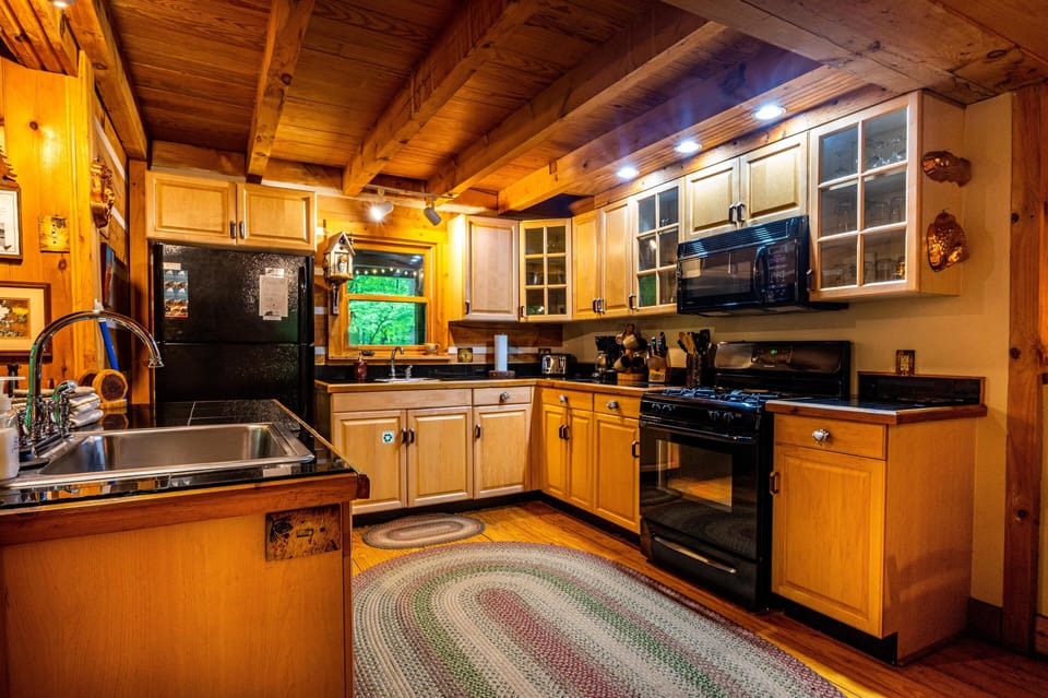 Kitchen with honey-toned cabinetry, black appliances, granite countertops, and a braided oval rug on wood floors.