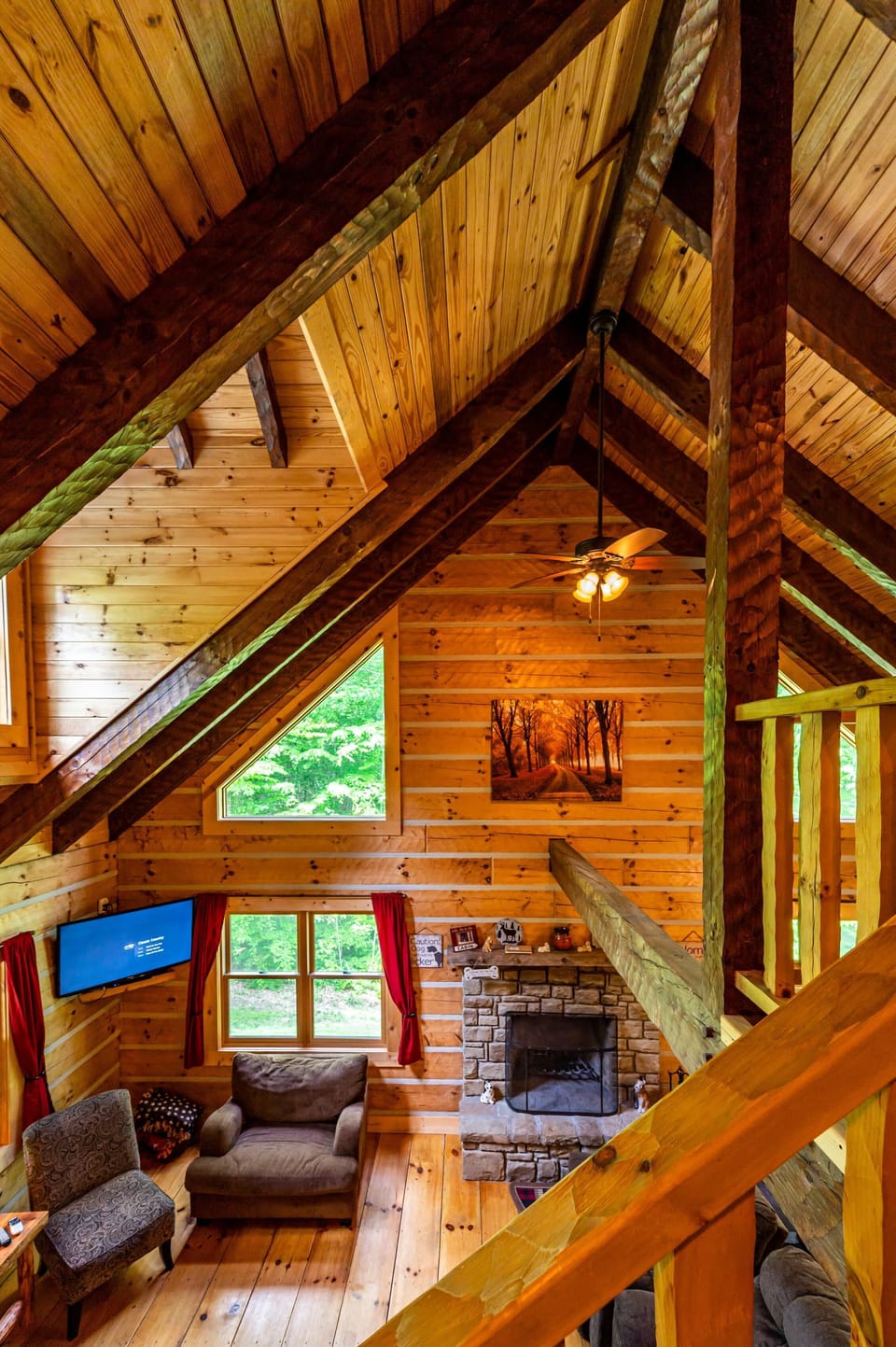 Vaulted wood ceilings with exposed beams hover above a stone fireplace and seating area with forest views.
