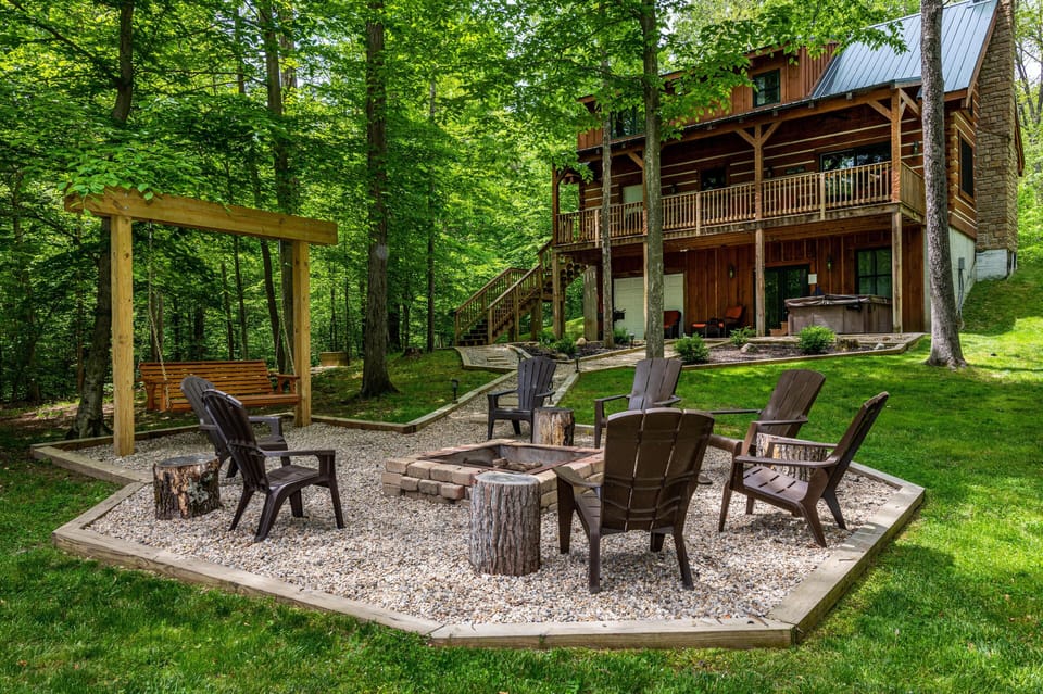 Outdoor fire pit area with brown Adirondack chairs, tree stump seats, and a wooden porch swing nearby.