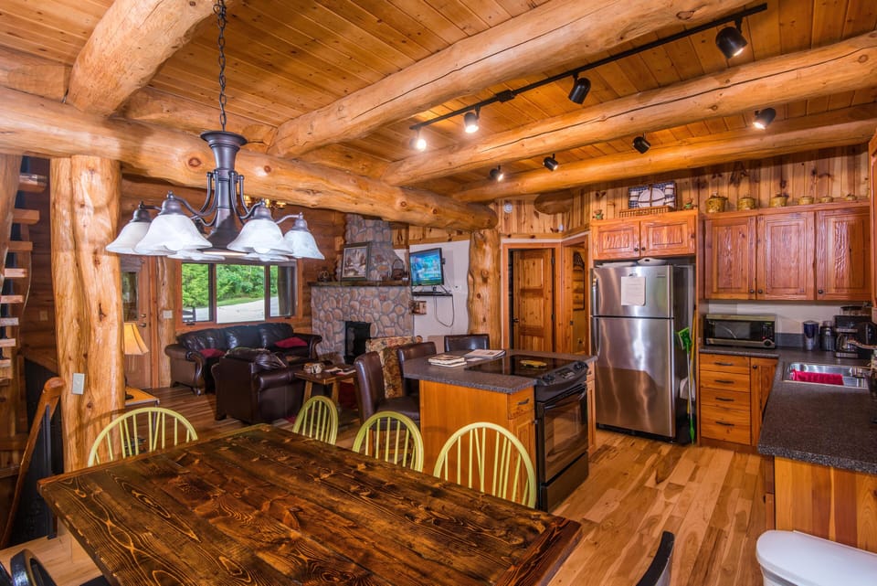 Rustic kitchen and dining area with knotty pine cabinets, stainless steel appliances, and a dark wood table.