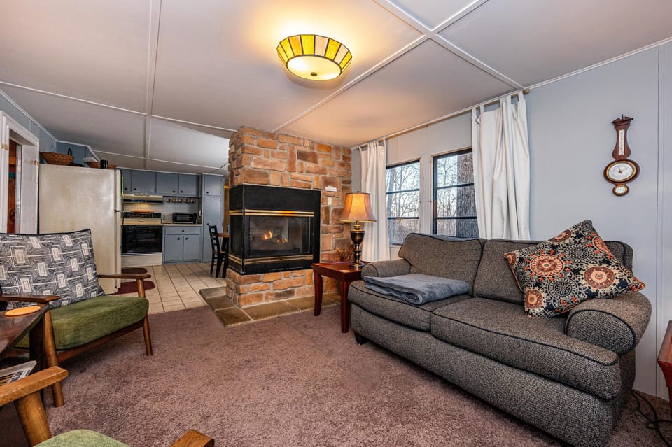 Fireplace with stone surround separates carpeted living area and tile-floored kitchen with blue cabinetry.