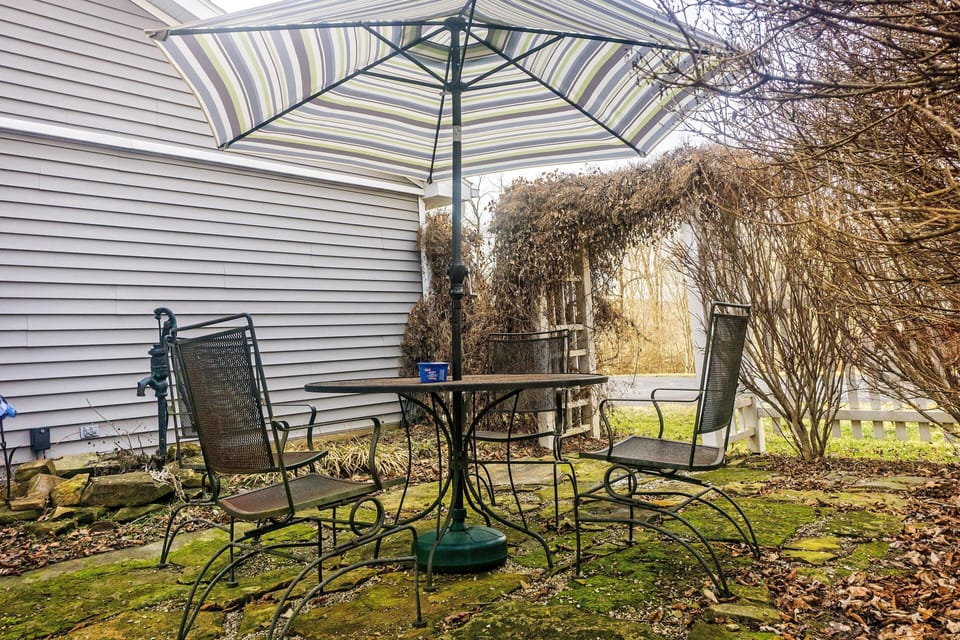 Metal patio chairs surround a round table with a striped umbrella on a mossy stone patio.
