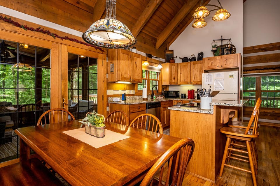 Wood dining table and bench sit beside granite-topped kitchen island with two wooden bar stools.