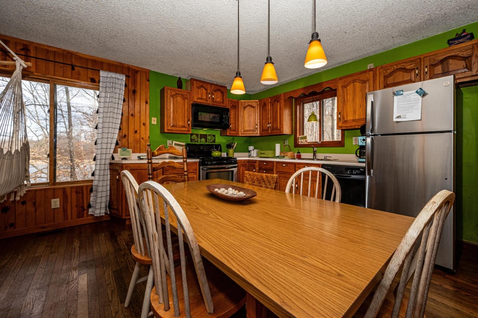 Orange pendant lights glow over the wooden dining table and mixed wood chairs in the kitchen.