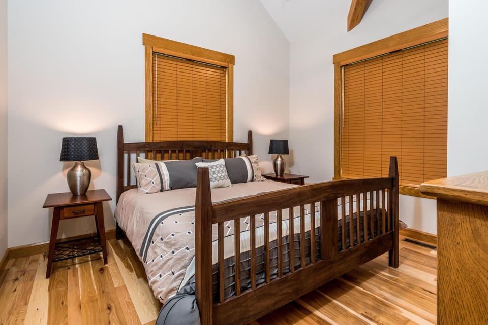 Wood-framed bed with patterned bedding sits between matching nightstands and lamps on natural hardwood floors.