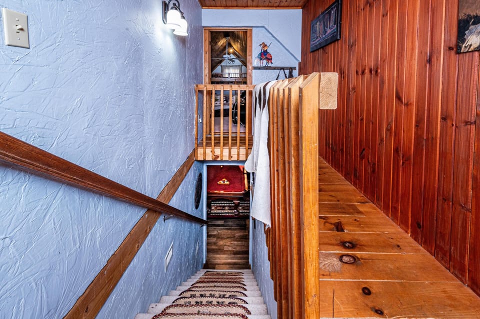 Carpeted staircase with patterned runner descends between textured blue walls and wood-paneled railing and trim.