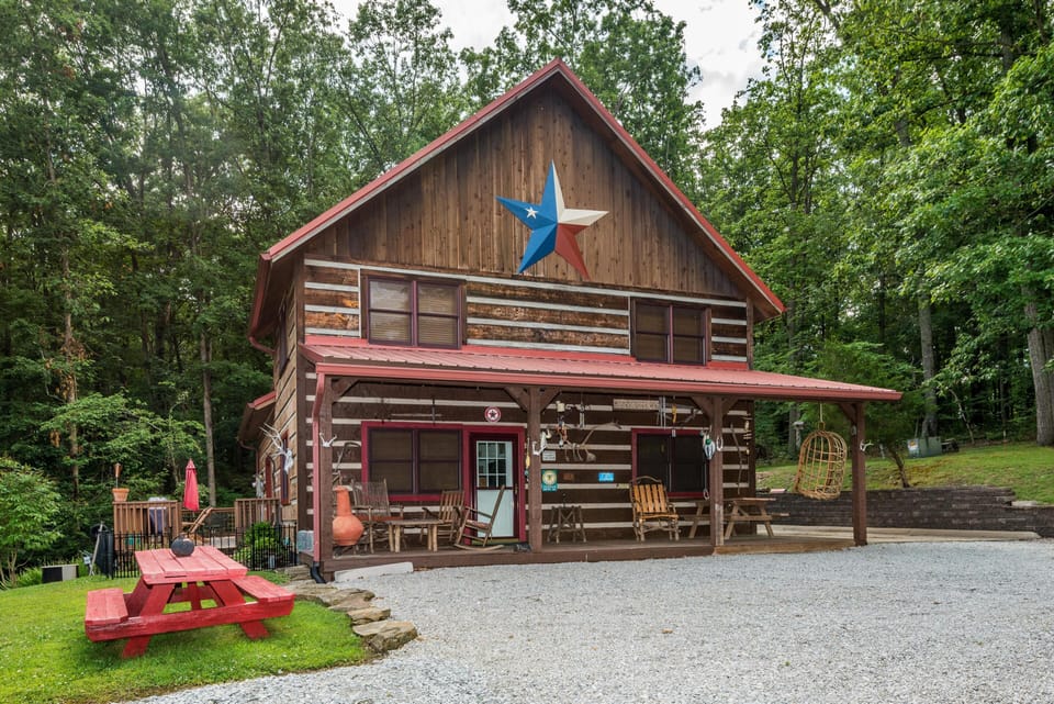Front porch features wooden rocking chairs, a hanging wicker swing, and a red picnic table on the lawn.