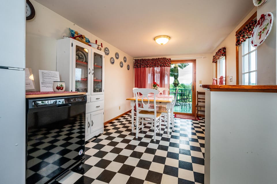 Dining area with black-and-white checkered floor, white wooden table and chairs, and red gingham curtains.