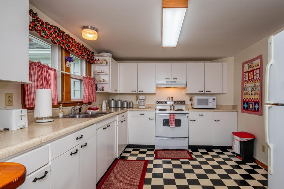Black-and-white checkered floor contrasts with white cabinetry and red gingham curtains in the kitchen.