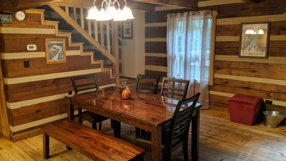 Polished wood dining table with black ladder-back chairs and bench under a multi-bulb chandelier.