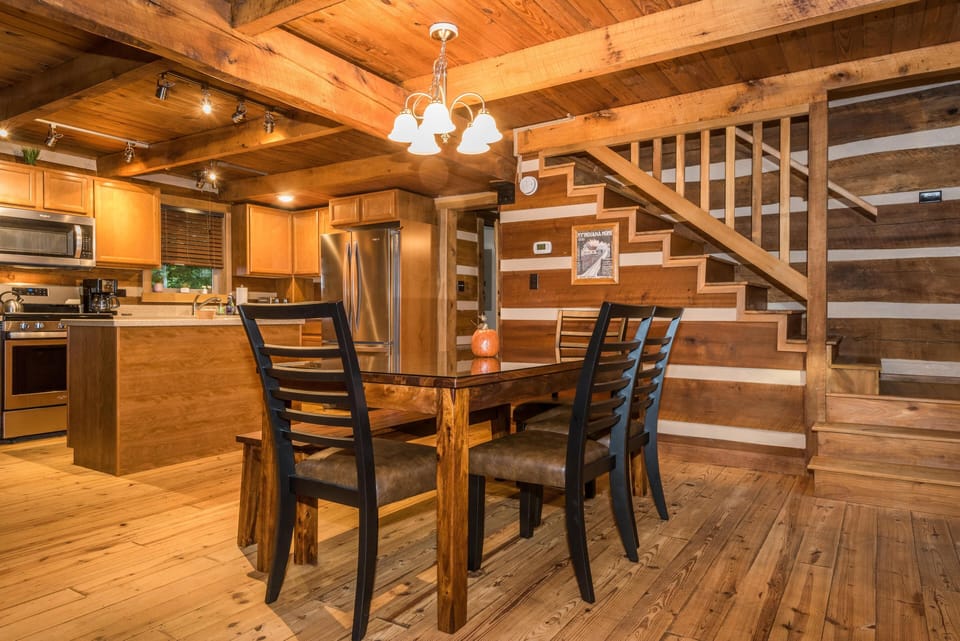 Dining area with a dark wood table, ladder-back chairs, and wood-paneled walls beside the staircase.