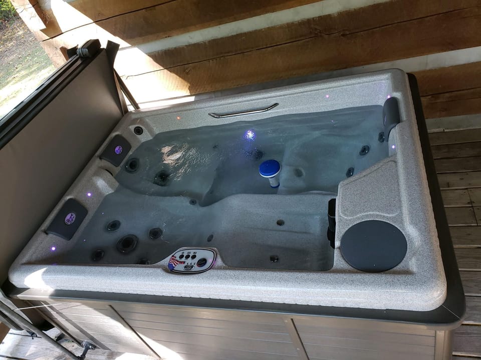Hot tub with built-in headrests, LED lights, and control panel, set against a wood-paneled wall.