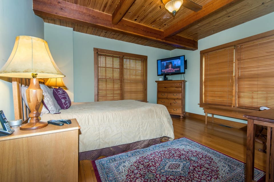Bedroom featuring exposed wood beams, hardwood floors, patterned area rug, and a mounted flat-screen TV.