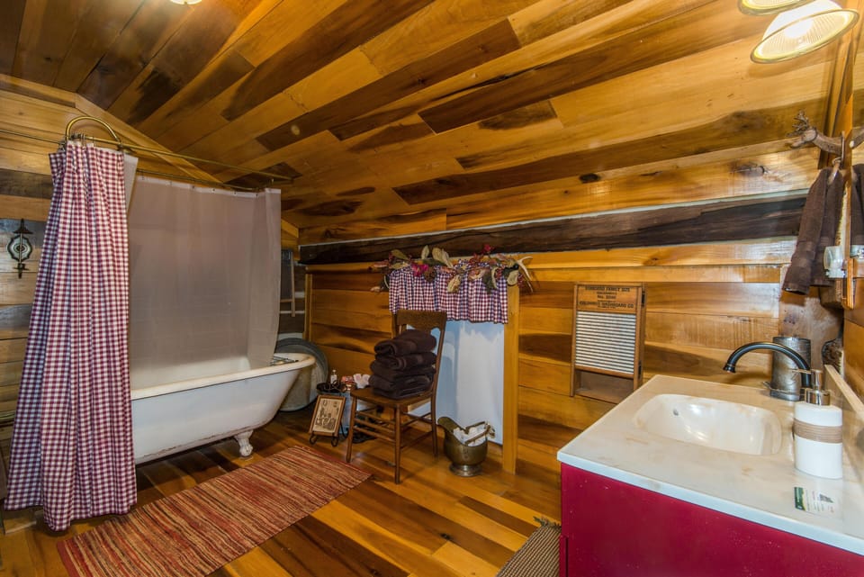 Bathroom with sloped wood-paneled ceiling, clawfoot tub with checkered curtain, and red vanity sink.