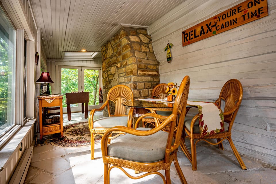 Natural light fills the sunroom with stone flooring, painted log walls, a foosball table, and a stone chimney centerpiece.