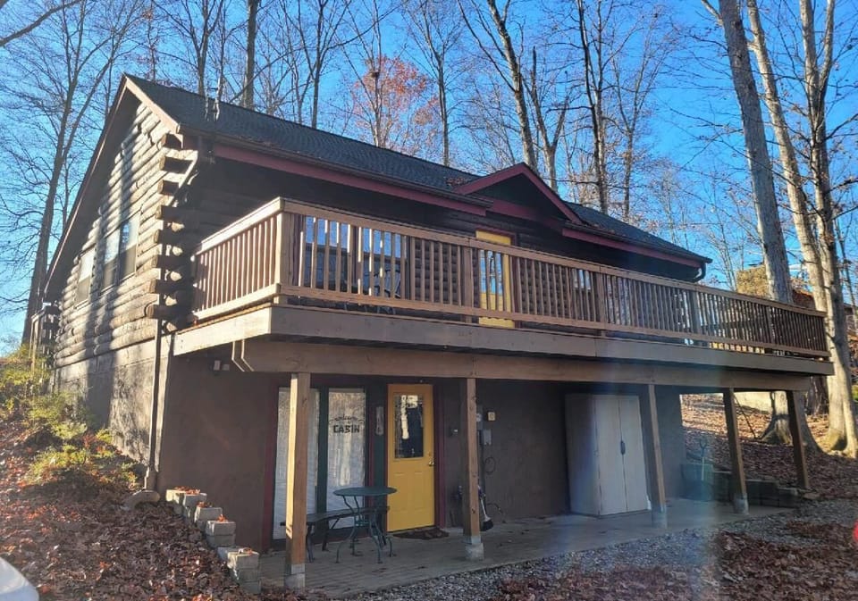 Exterior view showing natural wood siding, yellow front door, and wraparound upper deck railing.