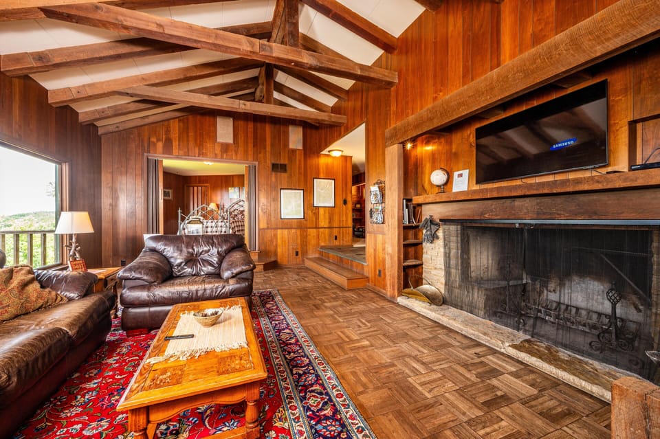 Leather sofas flank a wood coffee table atop a red patterned rug in the wood-paneled living room.