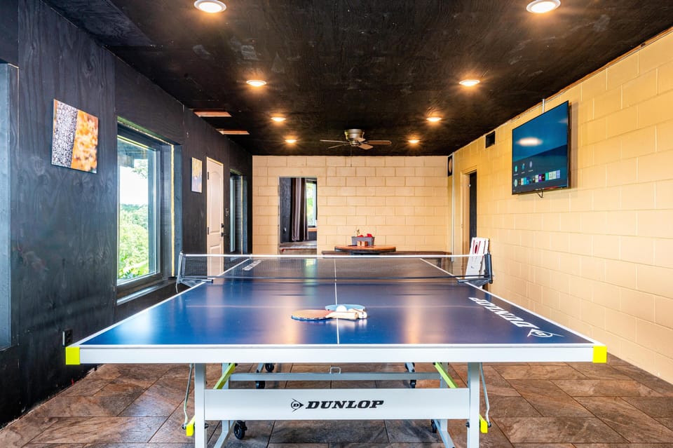 Game room with Dunlop ping pong table, tiled floor, black ceiling, yellow brick walls, and wall-mounted TV.