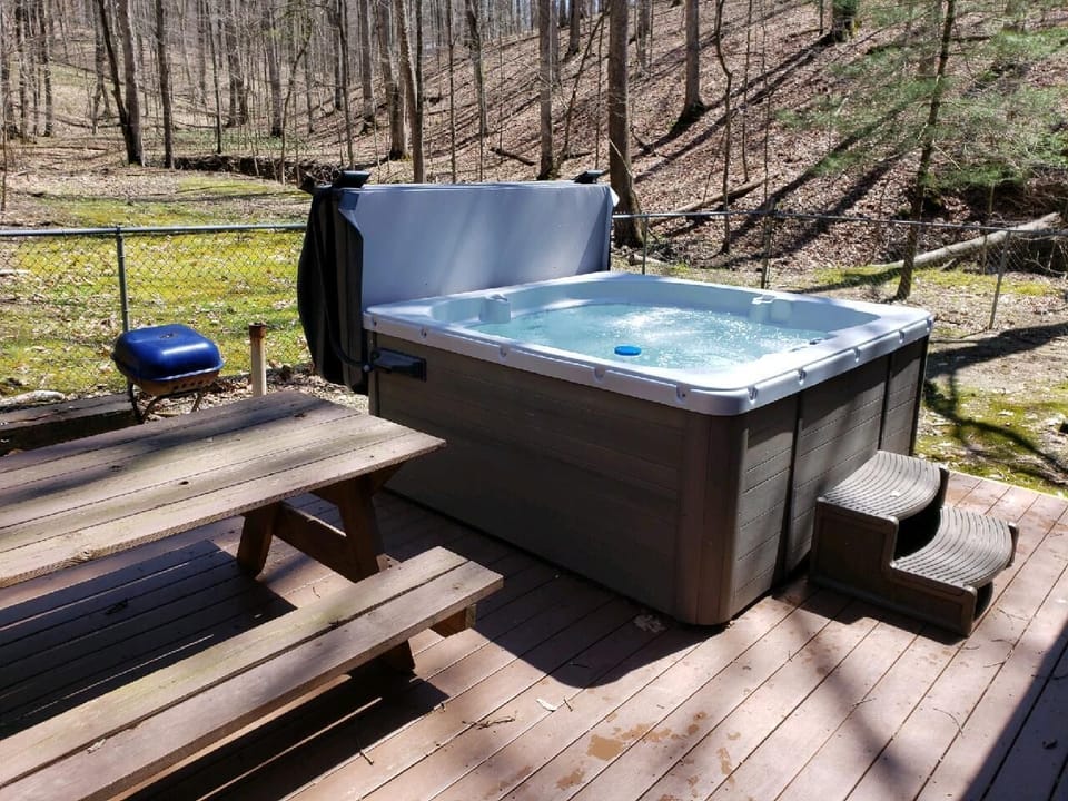 Outdoor hot tub bubbling beside a wooden picnic table and charcoal grill on the sunlit deck.