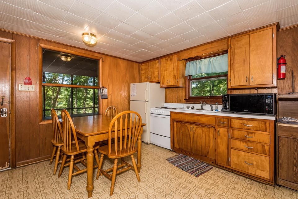 Wood-paneled kitchen features a four-chair dining table, white appliances, and a window with a blue valance.