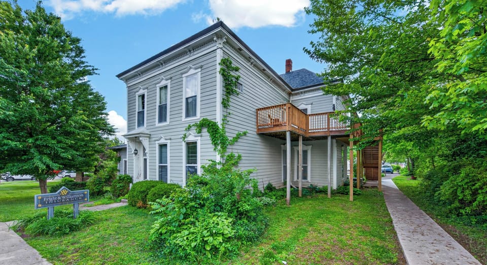 Exterior view of a two-story Victorian-style apartment with light gray siding, white trim, and a second-floor wooden balcony.