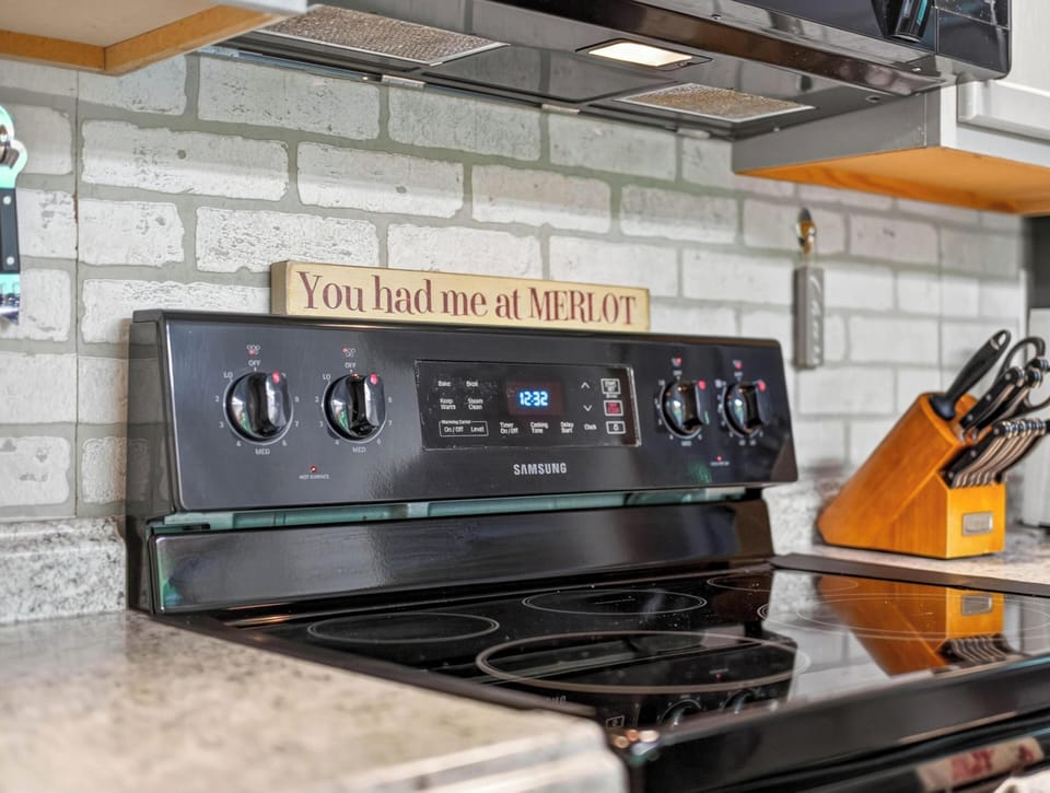 Electric stovetop with black glass surface sits below a microwave, against a white brick backsplash.