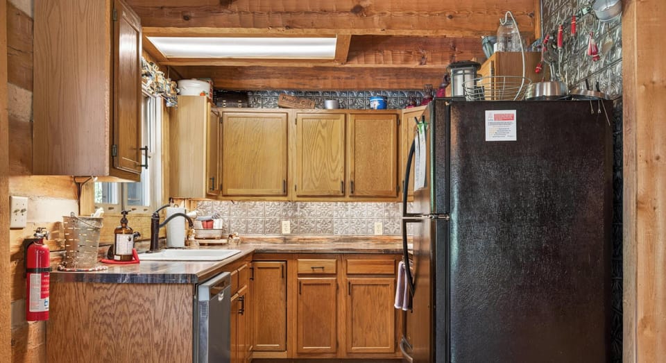 Wood-paneled kitchen features oak cabinets, black appliances, tin backsplash, and a skylight above the sink.
