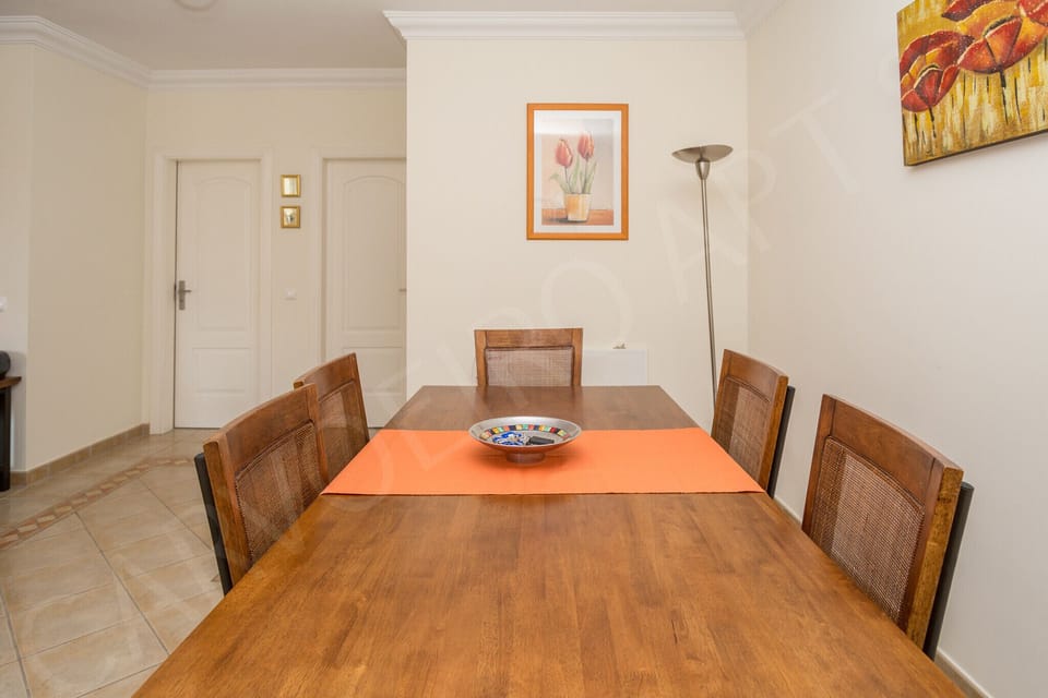 Dining area at Carvoeiro Apartment 8A with wooden table and chairs, framed artwork on the walls and a standing lamp, perfect for family meals in this 2-bedroom Algarve holiday apartment