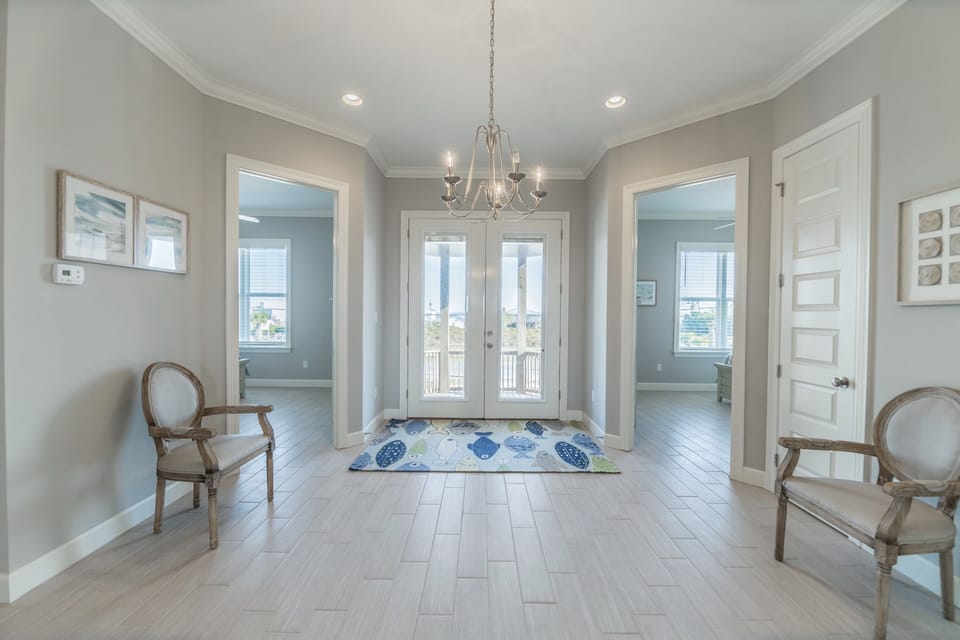 Bright, open foyer with elegant chandelier and beach-inspired accents. French doors and large windows fill the space with light, creating a welcoming entrance to your Dauphin Island vacation home.
