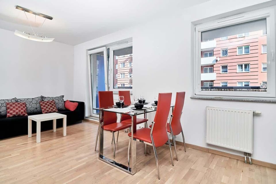 A bright living room with a black and red sofa, plus a red dining table and chairs near a large window.