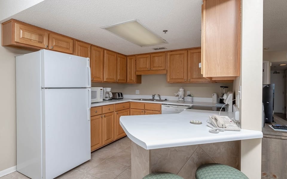 The fully-equipped kitchen features warm wood cabinetry, a breakfast bar with seating, and modern appliances for convenience