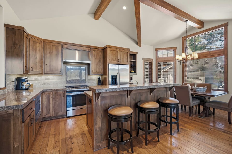 Gather in this open-concept kitchen with rustic wood cabinetry, granite countertops, and stainless steel appliances. Vaulted ceilings with exposed beams create a spacious, inviting atmosphere for your mountain getaway.