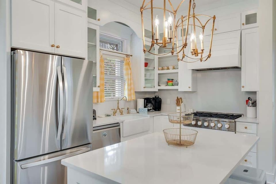 - White quartz island offers space to prep, serve, or gather for quick bites and conversation - Brass pendant lighting adds warmth and style to the bright kitchen layout - Stainless steel appliances pair with shaker cabinets for classic charm