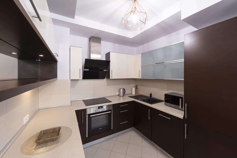 A modern kitchen with dark cabinets, a built-in oven, and a sleek countertop. Bright lighting enhances the space.