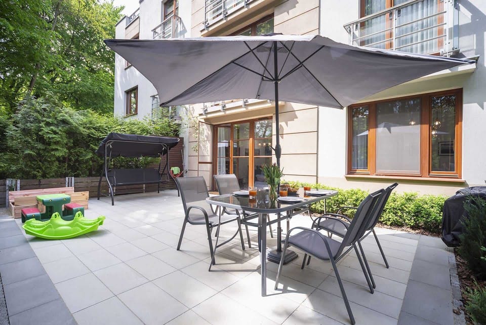 Another outdoor patio area, showing a table, chairs, and an umbrella. The greenery in the background adds a sense of privacy and relaxation.