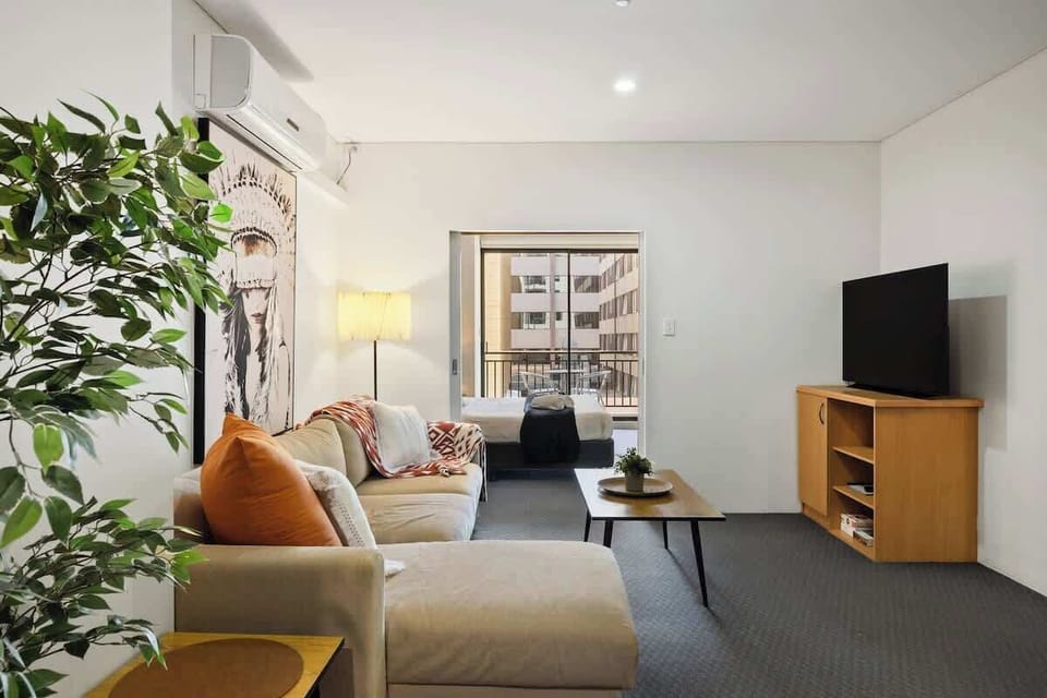 Your cozy home away from home. Unwind on the plush sofa, watch the flat-screen TV, or step onto the balcony for fresh air. The open layout offers a view of the comfy bed, with a touch of greenery to brighten the space.