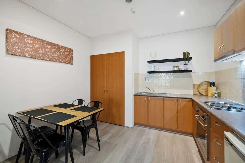 Enjoy meals at the cozy table for four, set with stylish placemats. Nearby, the kitchen has everything you need—wooden cabinets, a stove, an oven, a microwave, and a sink. Unique wall art adds a bit of charm.
