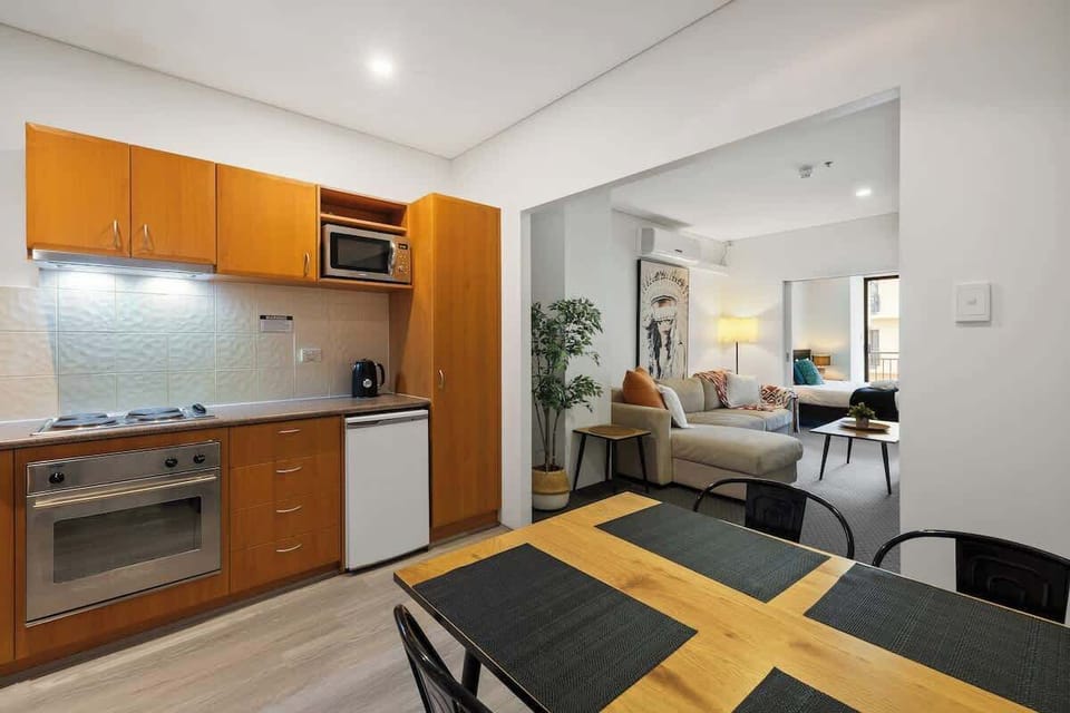 Your perfect home away from home! Relax in the cozy living area with stylish decor and a comfy sofa. Nearby, the kitchen has wooden cabinets, a stove, and modern appliances for a convenient stay.