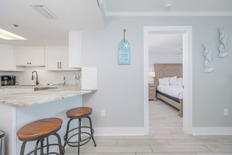 Open layout features a modern breakfast bar with seating, leading to the serene master bedroom and beach decor