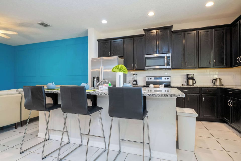 Sleek kitchen with dark cabinetry, stainless appliances, and a granite island with seating for four-open to the living room and that bold teal accent wall.