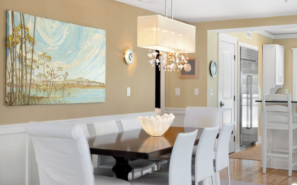 Gather around this elegant dining table for memorable meals, bathed in warm chandelier light with coastal artwork setting the scene.