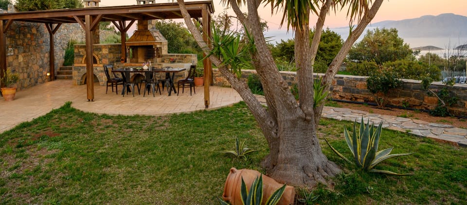 Εξωτερική τραπεζαρία με πέργκολα και πέτρινο BBQ.