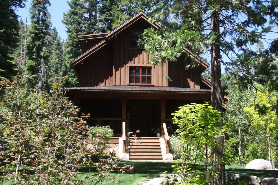 The main house with its covered front porch on the lawn, overlooking the forest
