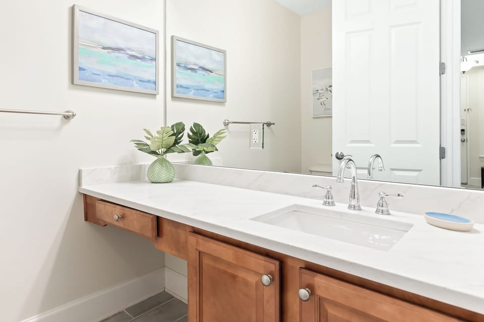 Refresh in your bright, stylish bathroom with coastal-inspired art, warm wood accents, and a pristine vanity designed for your comfort.