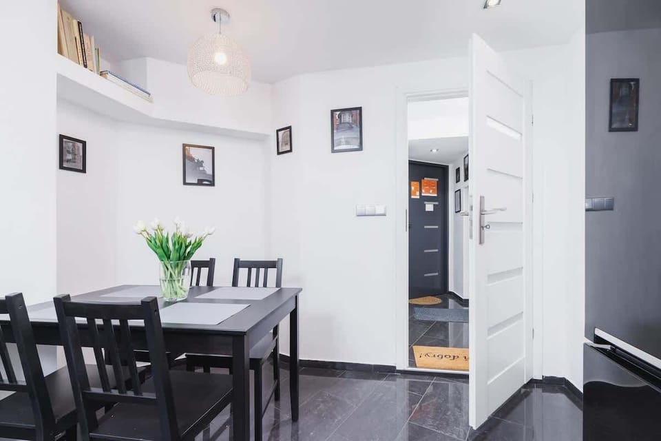 An open-plan area combining the living room and dining space, furnished with a modern table and chairs. Light walls and contrasting dark accents create a minimalist and functional atmosphere.