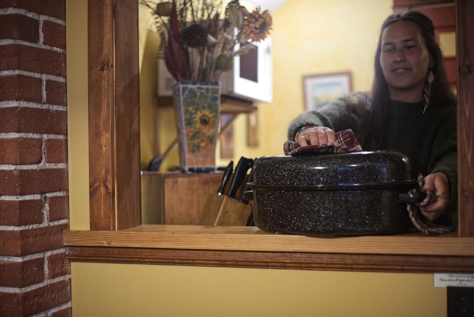 Kitchen pass-through with yellow walls, wooden trim, brick column, and a speckled roasting pan being handled.