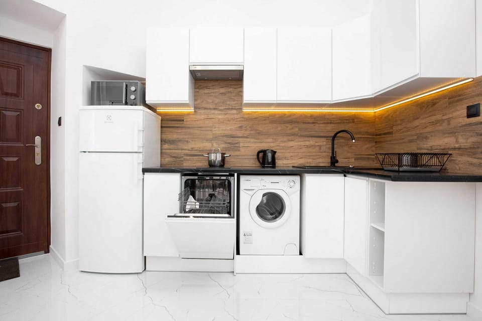 A bright and airy kitchen with white cabinets and a wood-accented countertop, blending modern aesthetics and functionality The kitchen has a dishwasher, washing machine and fridge.