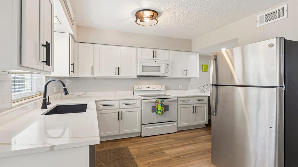 White shaker cabinets with black handles line the kitchen, paired with marble-patterned countertops and stainless steel appliances.