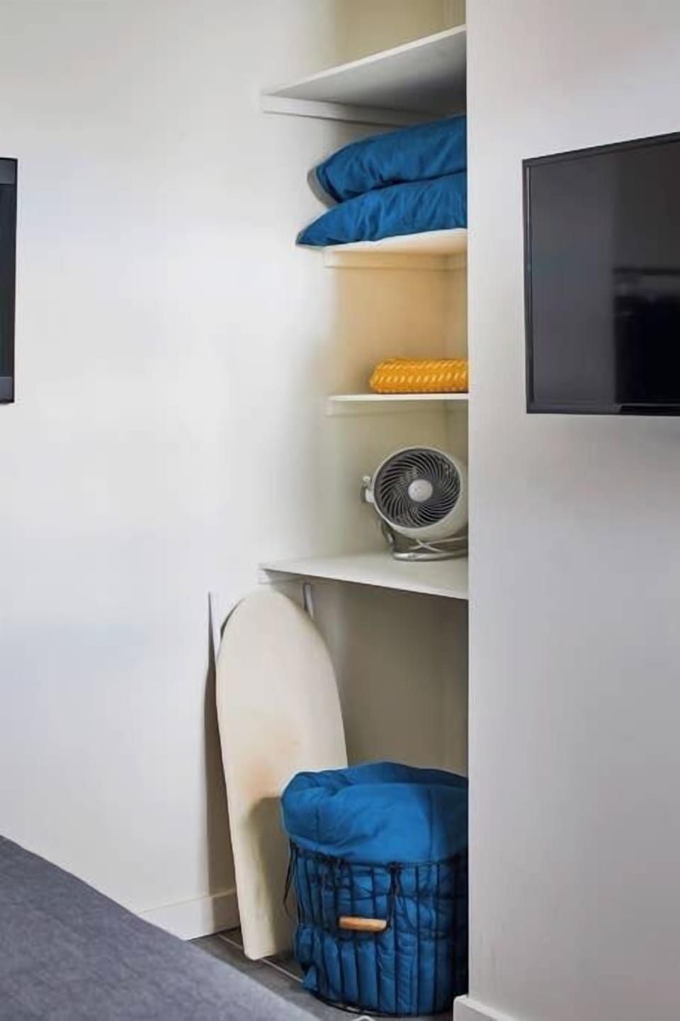 The corner shelves offer extra pillows and blankets, a fan and space heater, and a small iron and ironing board.