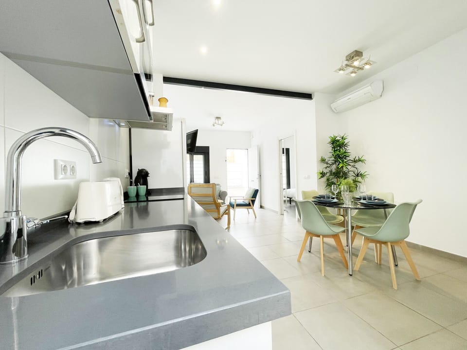 Linear kitchen of advanced design and maximum functionality, equipped with a quartz countertop and a steel sink, creating a fluid transition to the elegant dining area and living room in this modern open space.